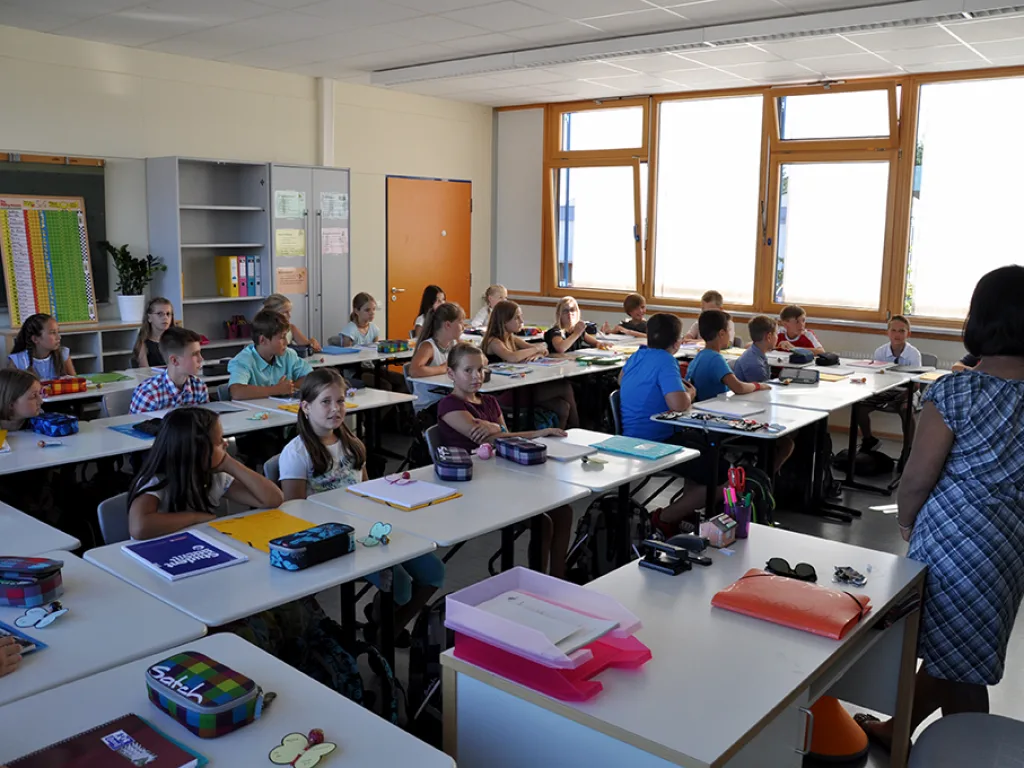 Blick durch den Klassenraum auf die Tischreihen mit Mäppchen und Heften.